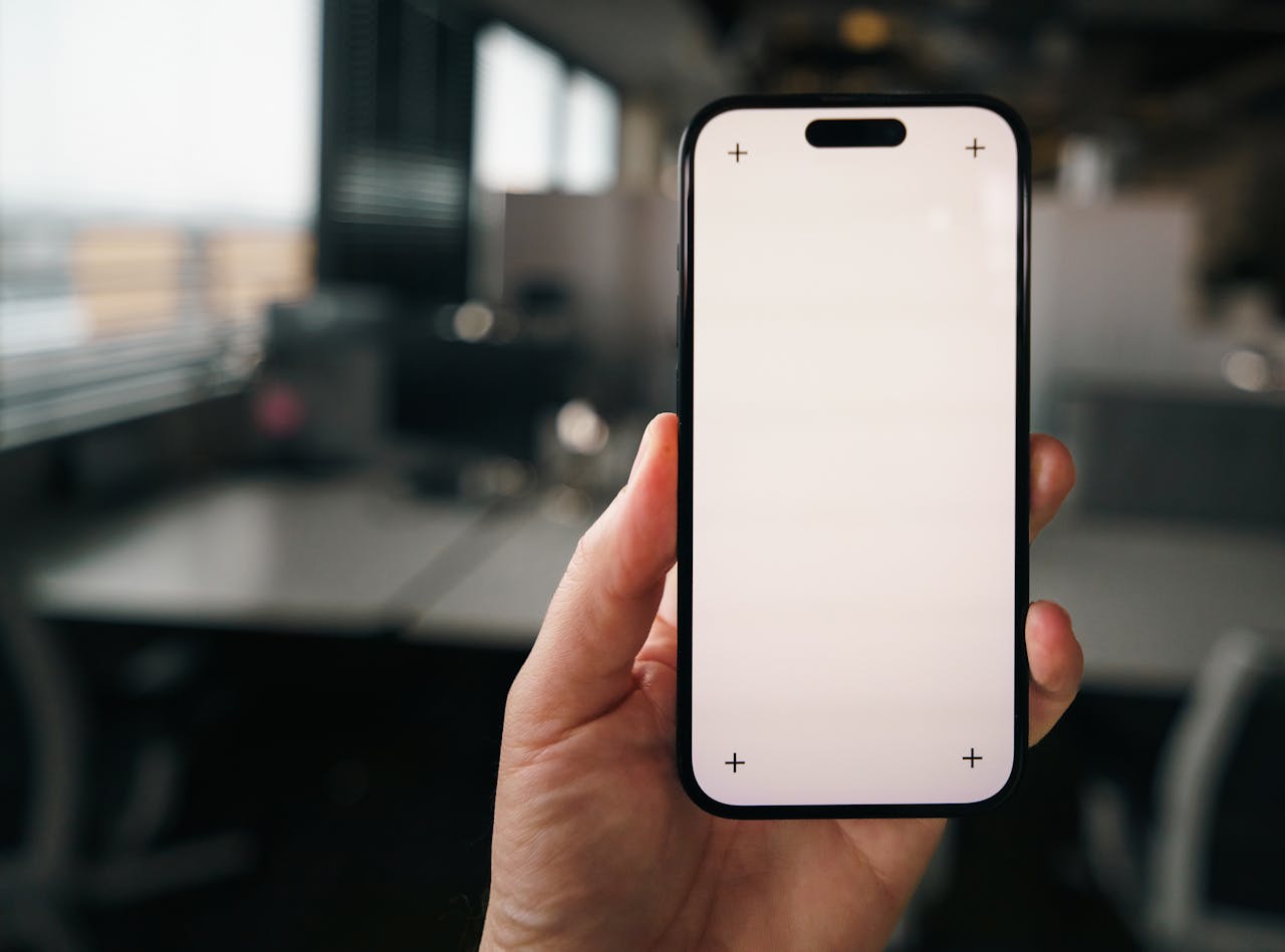 Hand holding a blank smartphone screen mockup in a modern office environment, perfect for apps showcasing.