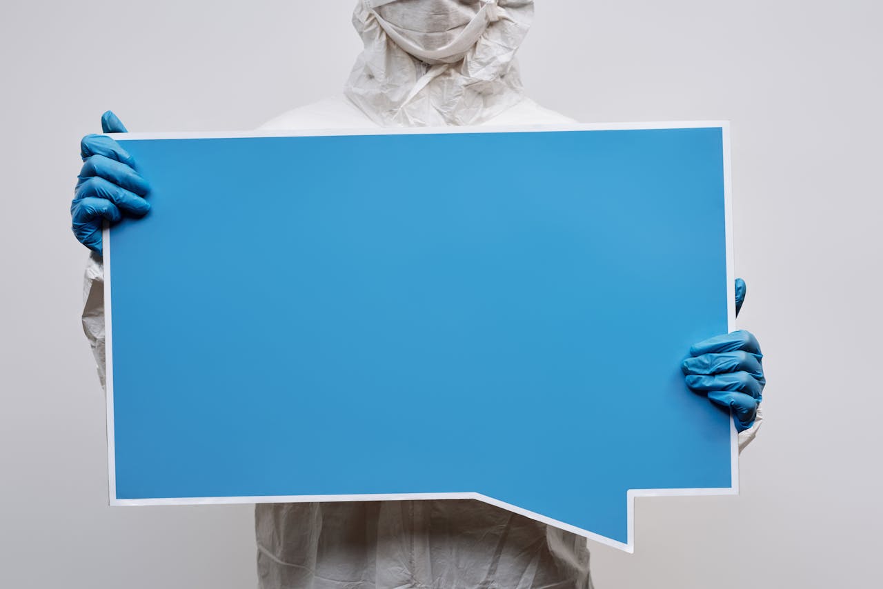 A person wearing protective gear holding a large blue speech bubble placard with copy space.